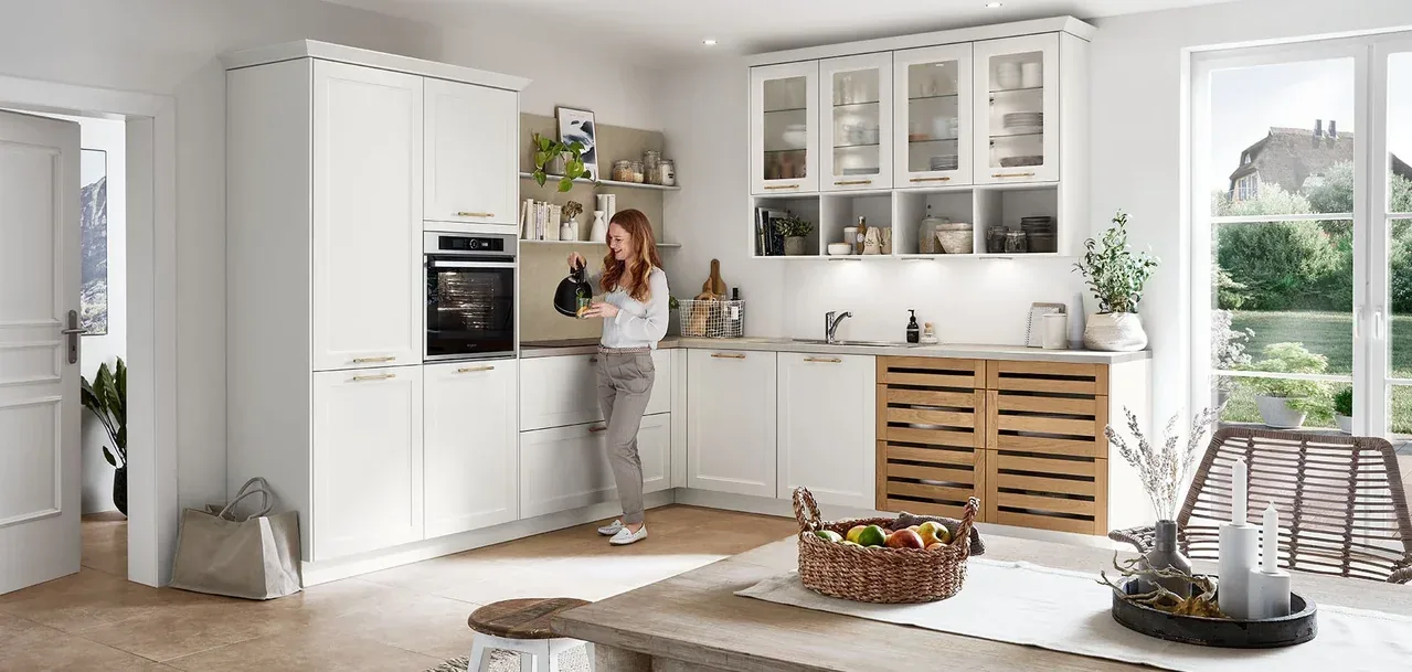 Cuisine en L blanche avec circulation dégagée, femme dans l’espace et vitrines vitrées