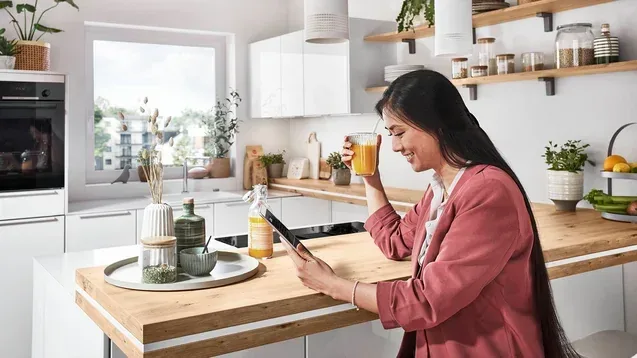 Femme buvant un jus à l’îlot d’une cuisine en U blanche avec coin repas bois