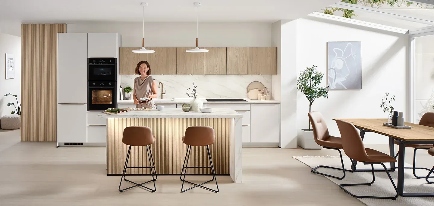 Cuisine ouverte style scandinave bois clair et blanc avec femme derrière l’îlot central