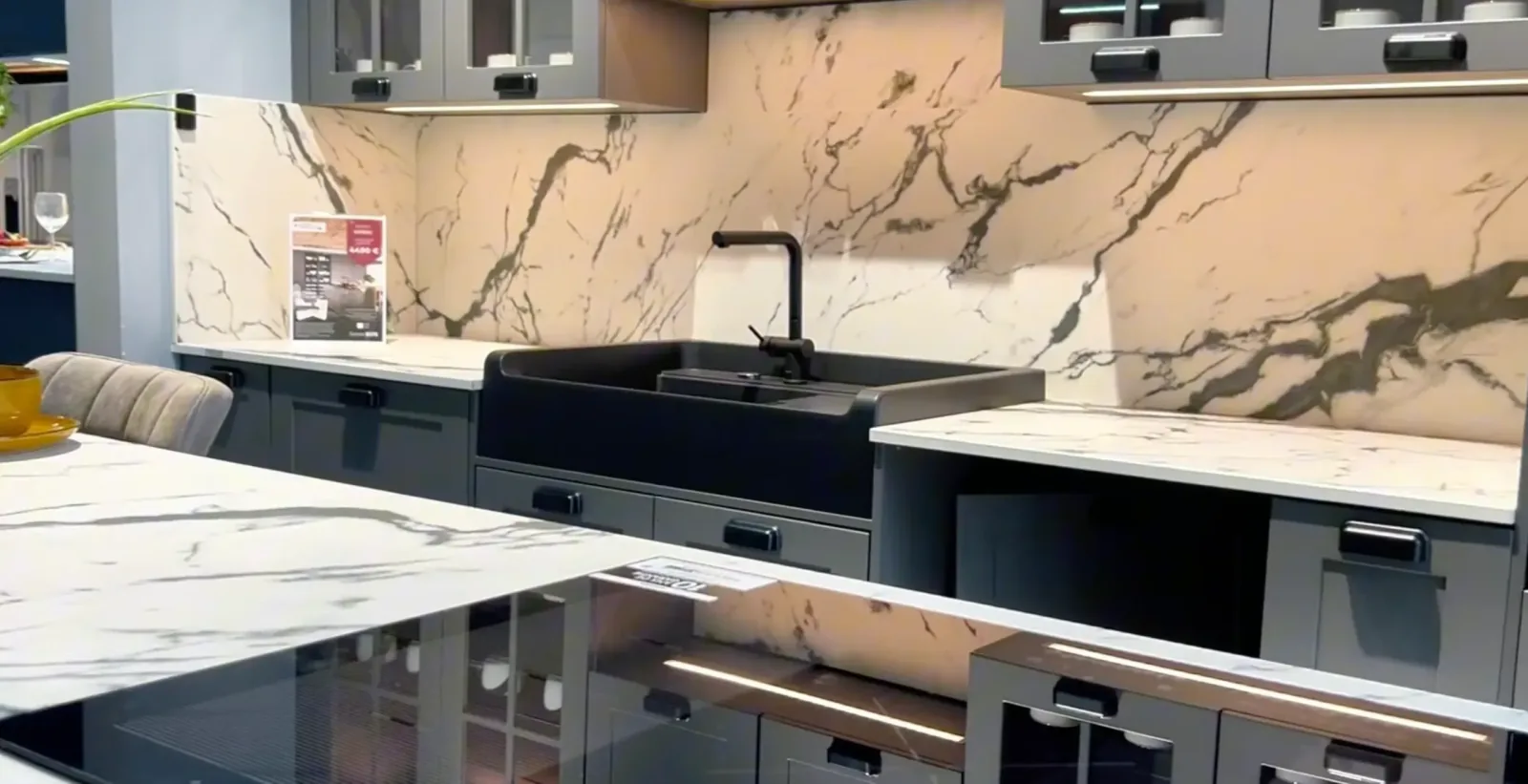 Cuisine showroom avec plan de travail et crédence en marbre veiné, évier noir et façades grises
