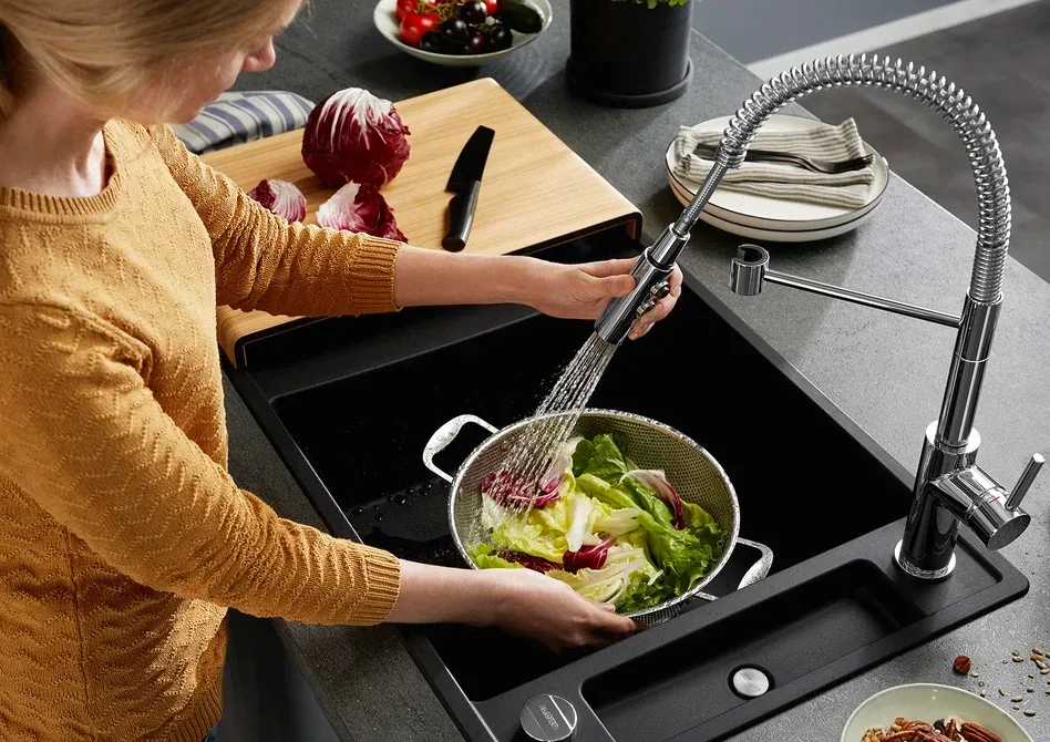Femme rinçant de la salade dans un évier Blanco noir avec mitigeur professionnel à douchette
