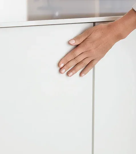 Main effleurant une façade de cuisine blanche ton neutre au design intemporel