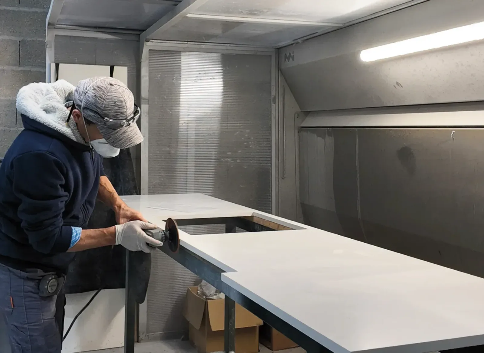 Marbrier Cuisines ELITE ponçant un plan de travail blanc dans l’atelier de production