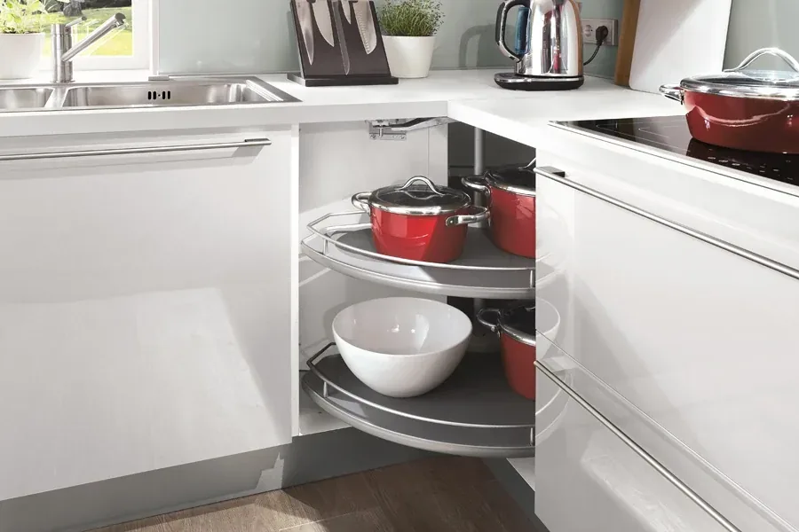 Meuble d’angle tourniquet blanc avec plateaux tournants et casseroles rouges rangées