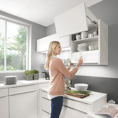 Femme ouvrant un meuble haut à porte relevable dans une cuisine blanche caisson XL