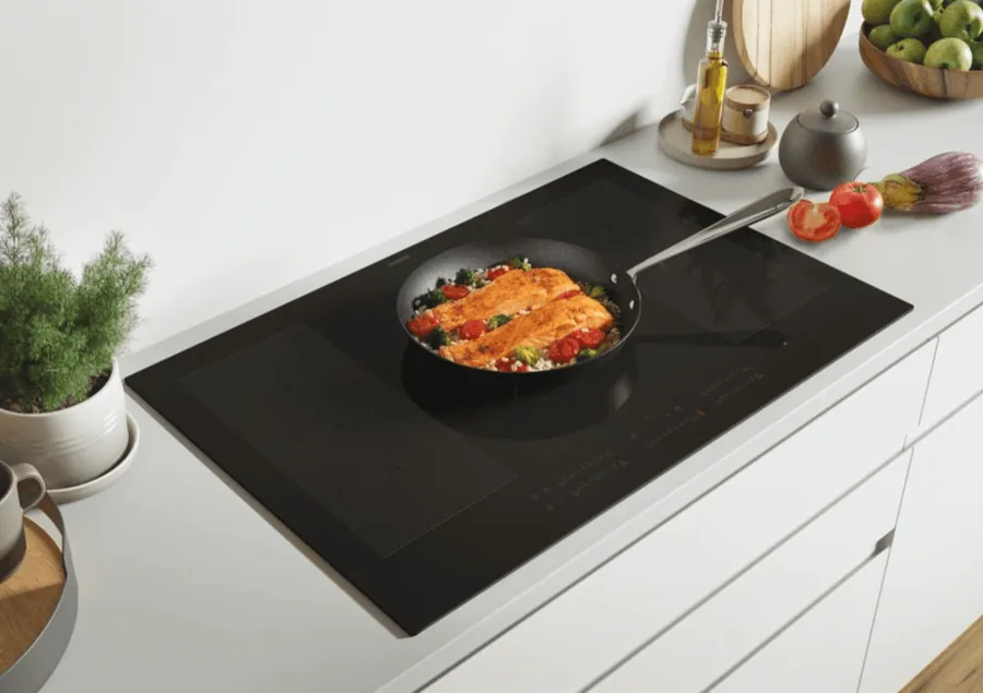 Table de cuisson induction Rosières noire avec bandeau de commandes tactiles, poêle de saumon et légumes en cuisson
