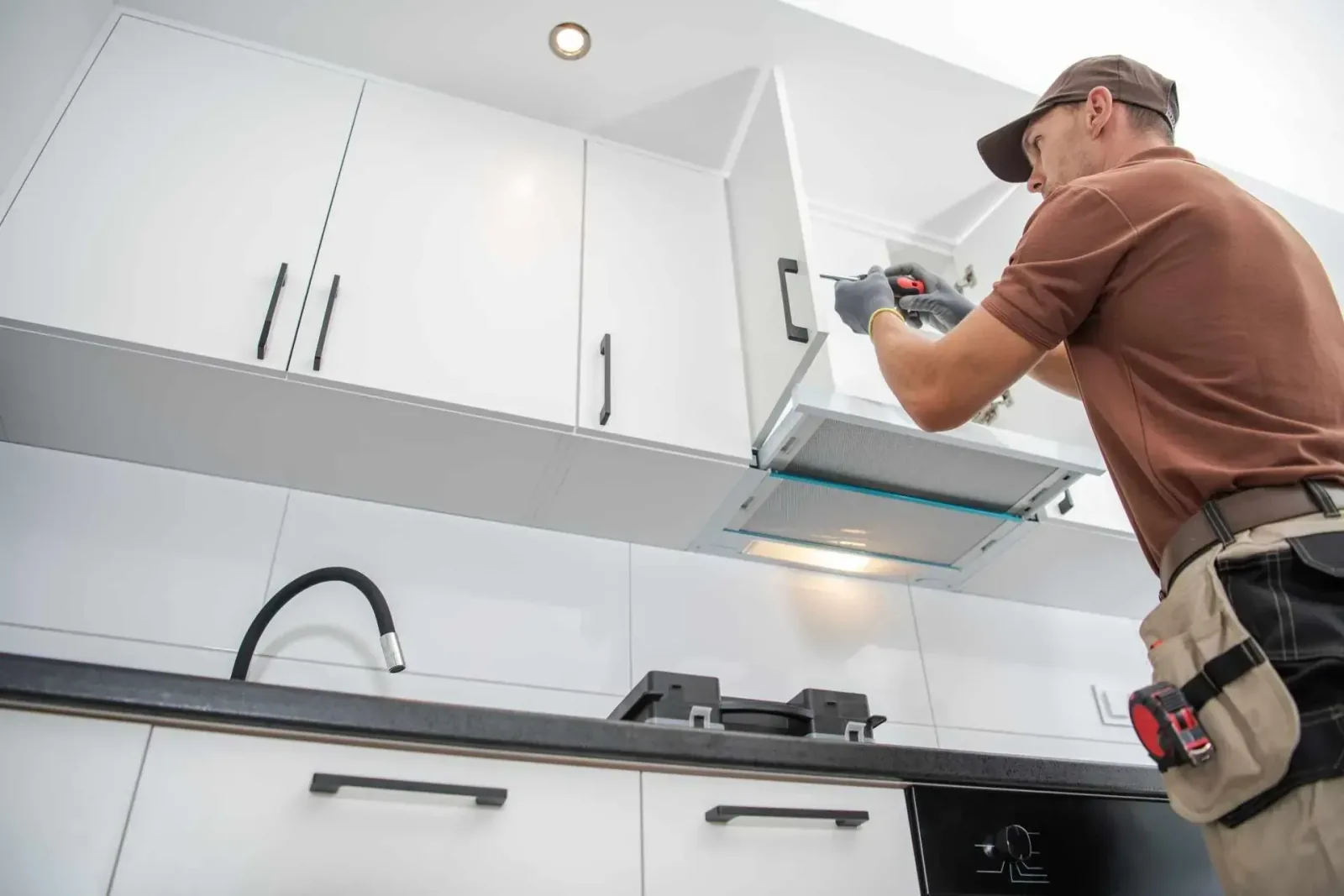 Technicien installant une hotte de cuisine encastrée dans un meuble blanc