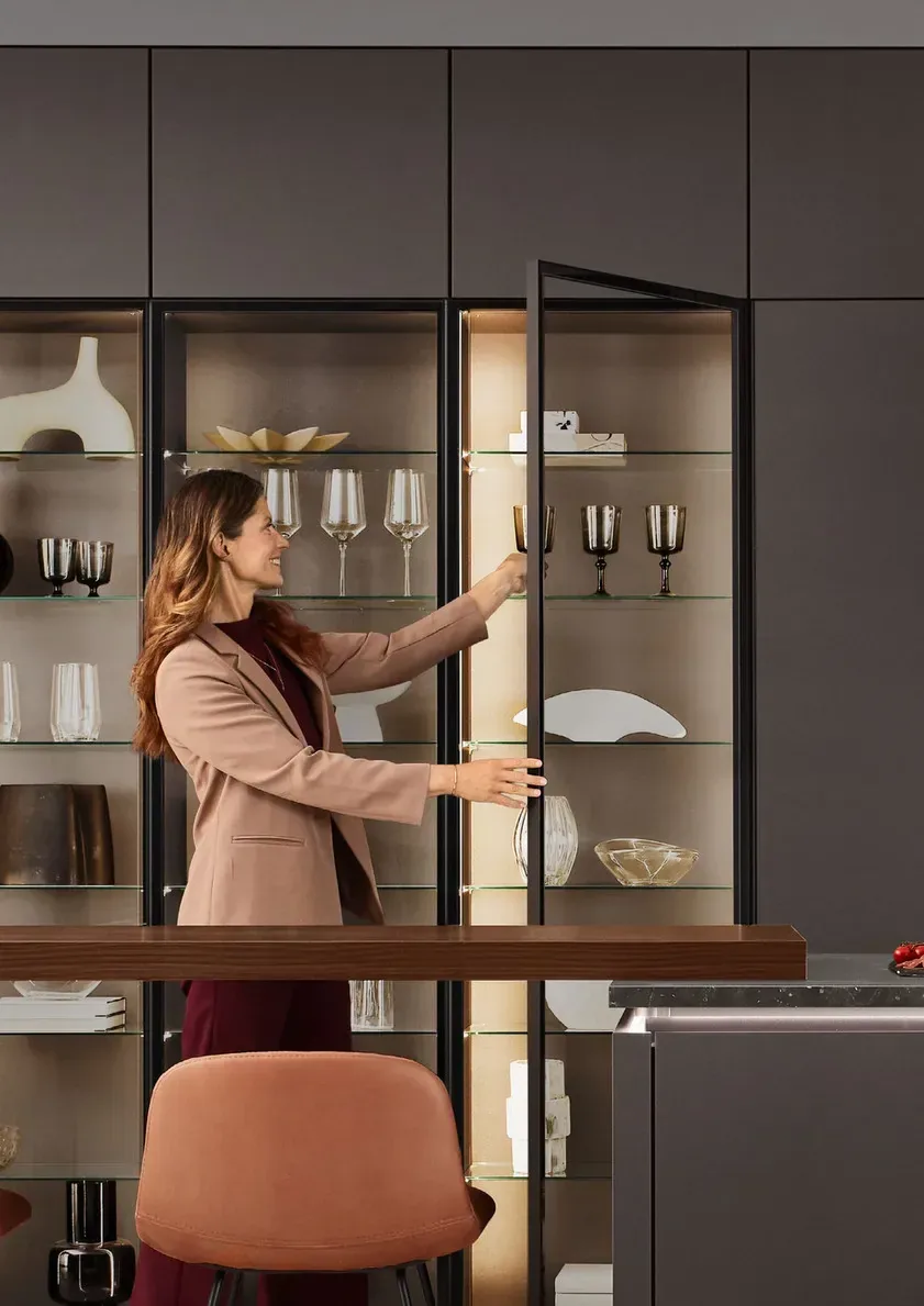 Femme rangeant des verres décoratifs dans la vitrine éclairée d’une cuisine grise